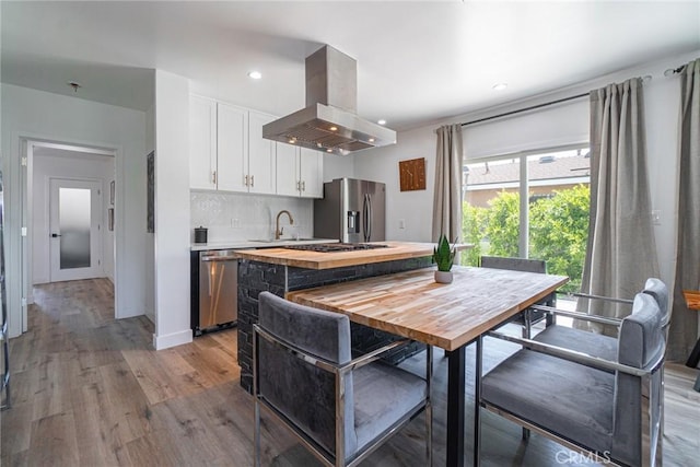 kitchen with white cabinets, a kitchen island, stainless steel appliances, island range hood, and butcher block countertops