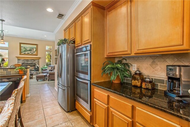 kitchen featuring appliances with stainless steel finishes, decorative light fixtures, a stone fireplace, dark stone countertops, and light tile patterned flooring