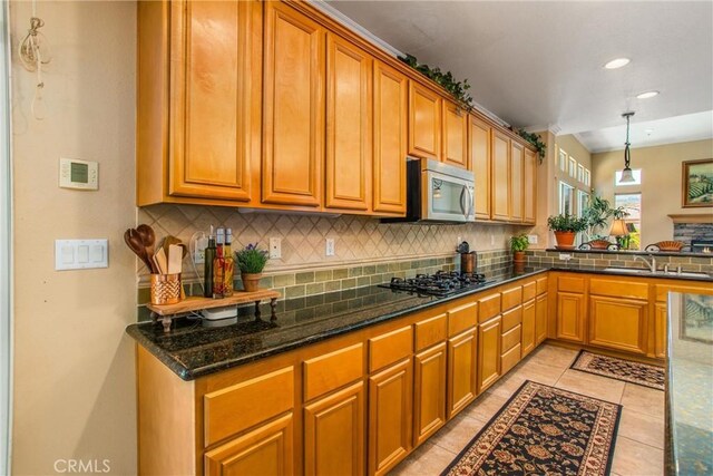 kitchen featuring light tile patterned floors, gas stovetop, dark stone counters, pendant lighting, and sink