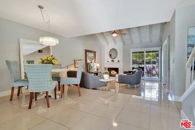 dining space with ceiling fan with notable chandelier, light tile patterned floors, lofted ceiling with beams, and a fireplace