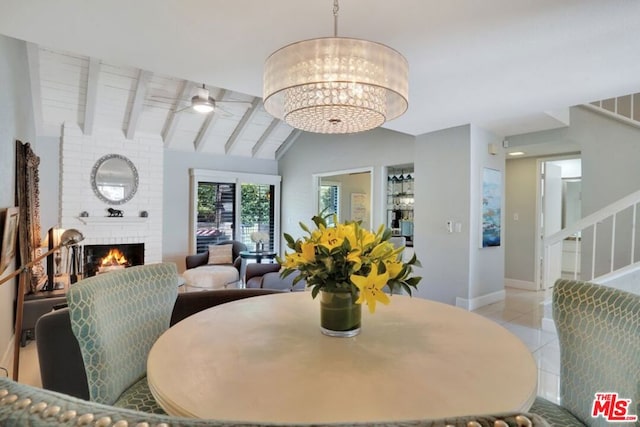 dining room with a brick fireplace, ceiling fan with notable chandelier, light tile patterned floors, and vaulted ceiling with beams