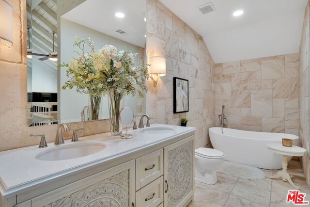 bathroom featuring ceiling fan, a tub to relax in, lofted ceiling, tile walls, and vanity