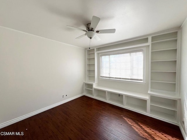 spare room with ceiling fan, built in shelves, and dark hardwood / wood-style flooring