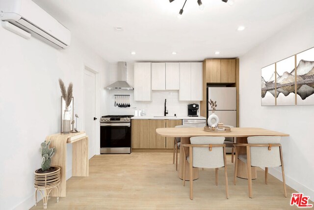 kitchen featuring an AC wall unit, wall chimney range hood, sink, stainless steel stove, and backsplash