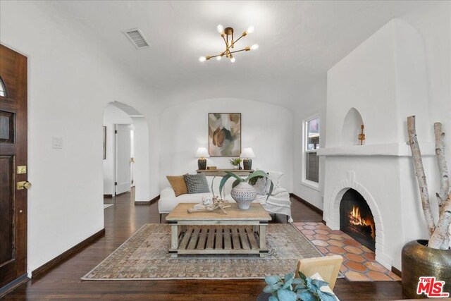 living room with dark wood-type flooring, a fireplace, and a chandelier