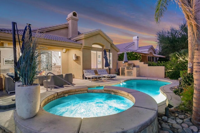 pool at dusk with an outdoor kitchen, an in ground hot tub, and a patio