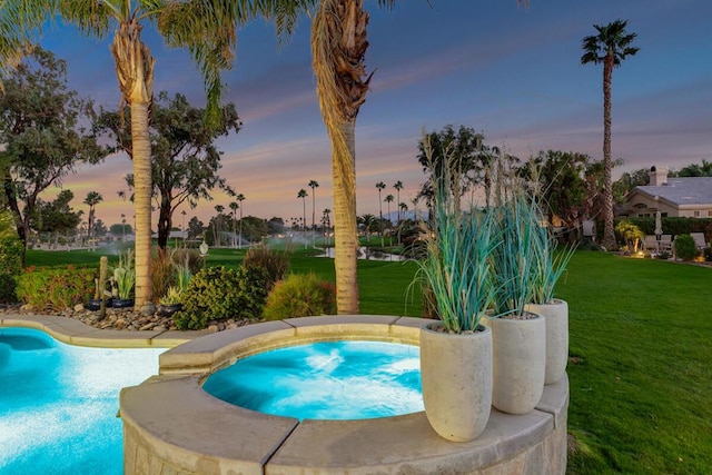 pool at dusk with an in ground hot tub and a yard