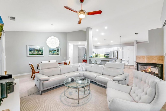 living room with light carpet, ceiling fan, vaulted ceiling, and a tiled fireplace