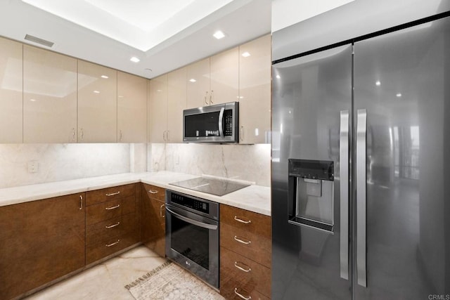 kitchen featuring tasteful backsplash, cream cabinetry, light stone counters, and stainless steel appliances