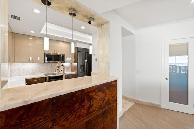 kitchen with decorative light fixtures, backsplash, light wood-type flooring, light stone countertops, and appliances with stainless steel finishes