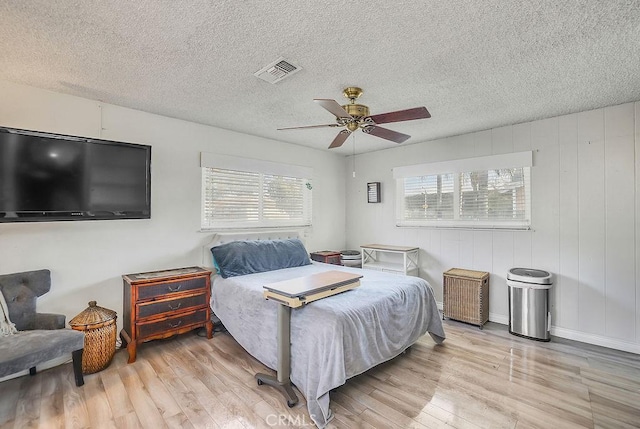 bedroom featuring ceiling fan, multiple windows, light hardwood / wood-style flooring, and a textured ceiling