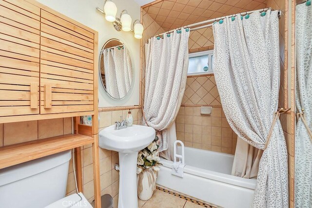 full bathroom featuring toilet, shower / bath combo with shower curtain, tile patterned flooring, tile walls, and sink