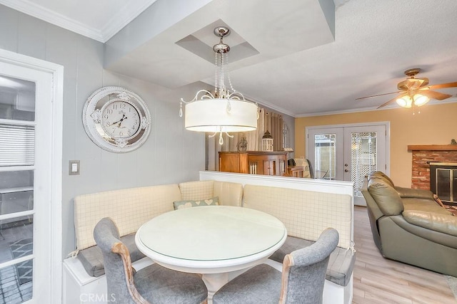 dining area with french doors, a fireplace, ceiling fan, light hardwood / wood-style flooring, and crown molding