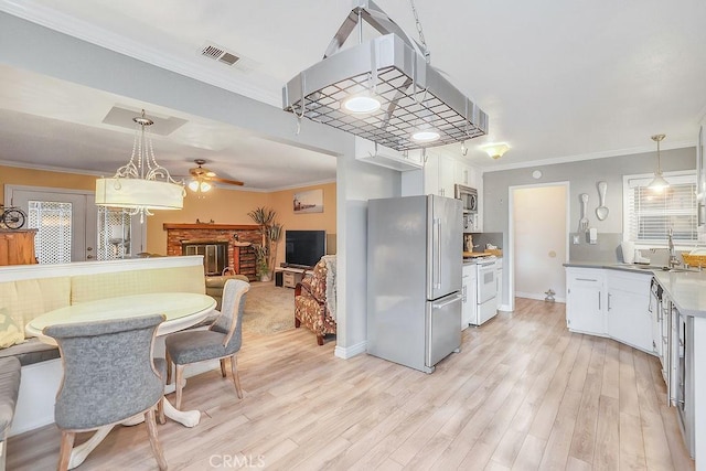 kitchen featuring a brick fireplace, appliances with stainless steel finishes, pendant lighting, and white cabinets