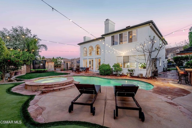 back house at dusk featuring a swimming pool with hot tub, a trampoline, and a patio