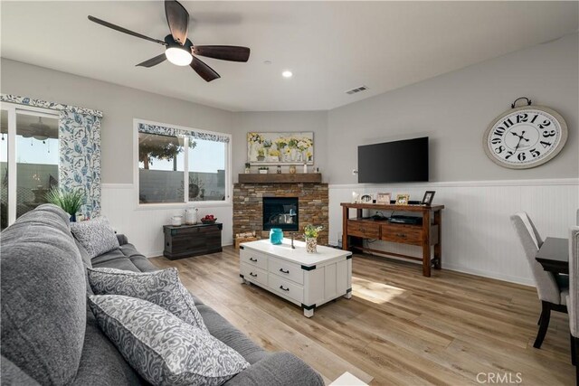 living room featuring ceiling fan, light hardwood / wood-style flooring, and a stone fireplace