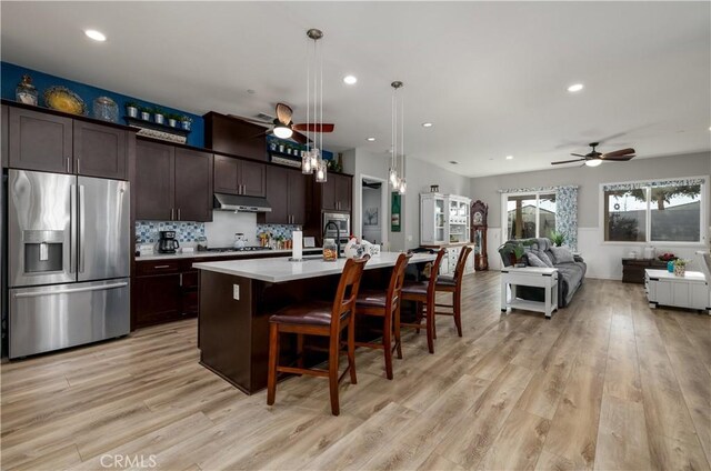 kitchen featuring light hardwood / wood-style flooring, decorative light fixtures, a kitchen bar, stainless steel appliances, and a center island with sink