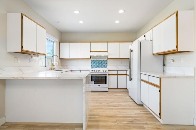 kitchen with white cabinetry, light hardwood / wood-style floors, kitchen peninsula, white appliances, and sink