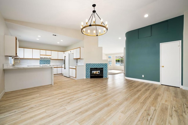 unfurnished living room featuring light wood-type flooring, sink, a tile fireplace, and a notable chandelier