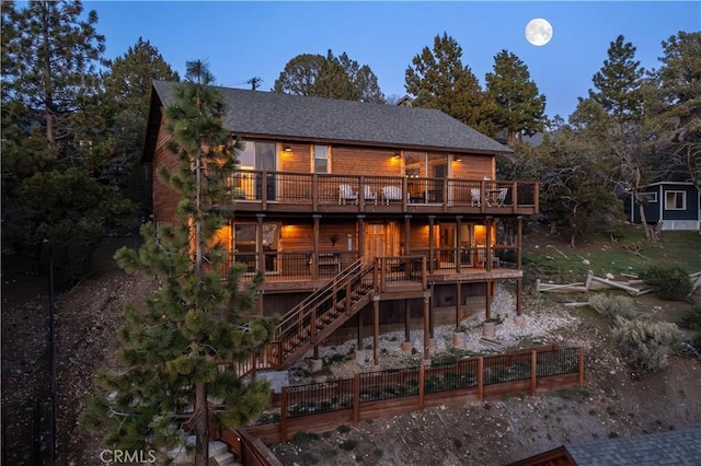 back house at dusk with a wooden deck and a balcony