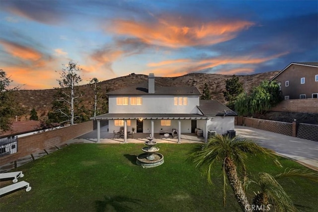 back house at dusk featuring a yard, a mountain view, and a patio area