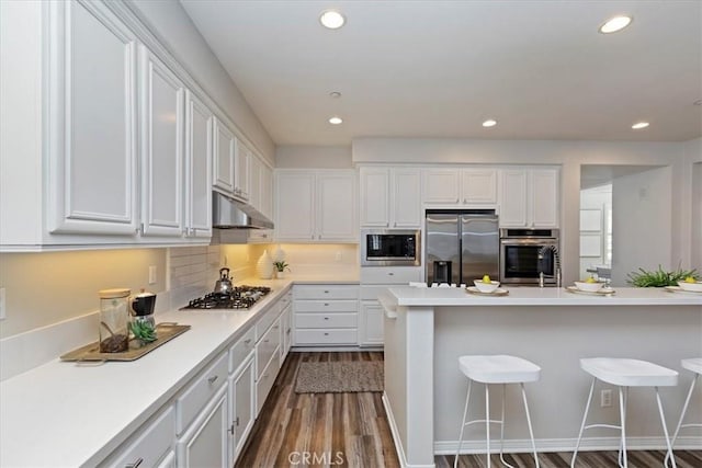 kitchen featuring stainless steel appliances, a kitchen bar, white cabinetry, and dark hardwood / wood-style floors