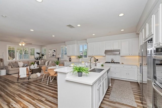 kitchen featuring stainless steel oven, white cabinets, a kitchen island with sink, and sink