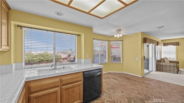 kitchen with ceiling fan, sink, black dishwasher, and tile counters