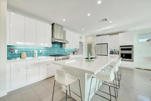 kitchen with wall chimney exhaust hood, sink, stainless steel appliances, and white cabinetry