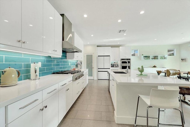 kitchen with appliances with stainless steel finishes, wall chimney exhaust hood, white cabinets, and sink