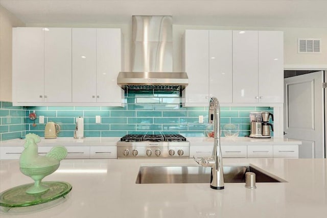 kitchen with backsplash, sink, wall chimney range hood, and white cabinets