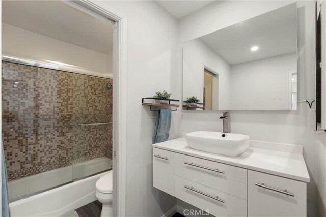 full bathroom with hardwood / wood-style flooring, combined bath / shower with glass door, vanity, and toilet