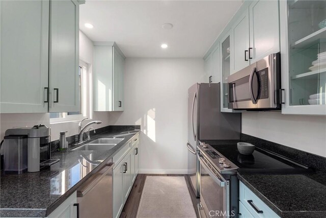 kitchen with white cabinets, appliances with stainless steel finishes, dark stone countertops, light hardwood / wood-style floors, and sink