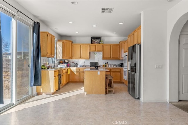 kitchen featuring white double oven, sink, black fridge, a breakfast bar area, and a kitchen island