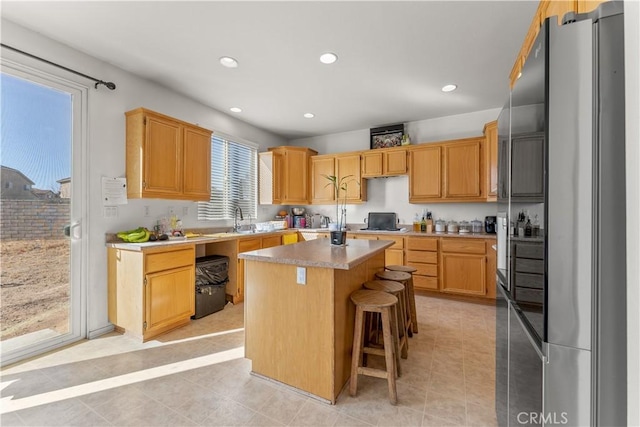 kitchen featuring sink, light tile patterned floors, a breakfast bar area, a kitchen island, and stainless steel refrigerator