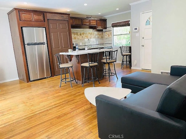 kitchen with a breakfast bar area, open floor plan, freestanding refrigerator, light countertops, and crown molding