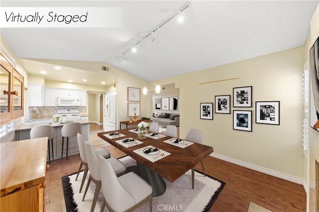 dining area featuring sink, lofted ceiling, wood-type flooring, and rail lighting