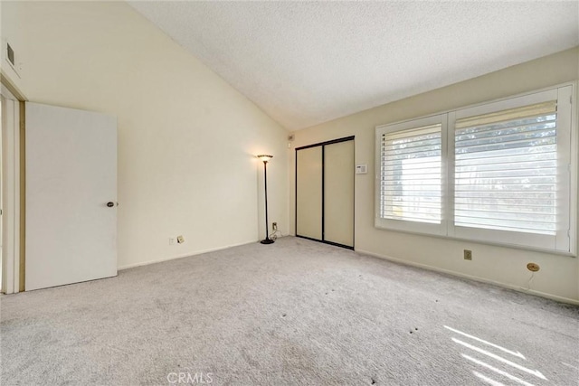 unfurnished bedroom with a textured ceiling, lofted ceiling, and light colored carpet