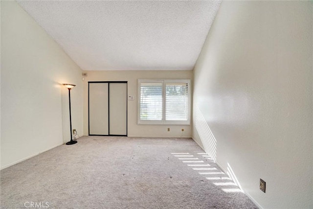 unfurnished bedroom with light colored carpet, a textured ceiling, and lofted ceiling