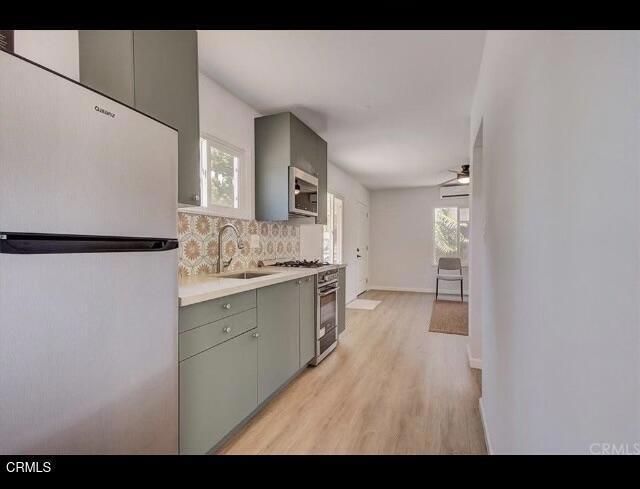 kitchen with sink, appliances with stainless steel finishes, light wood-type flooring, and tasteful backsplash