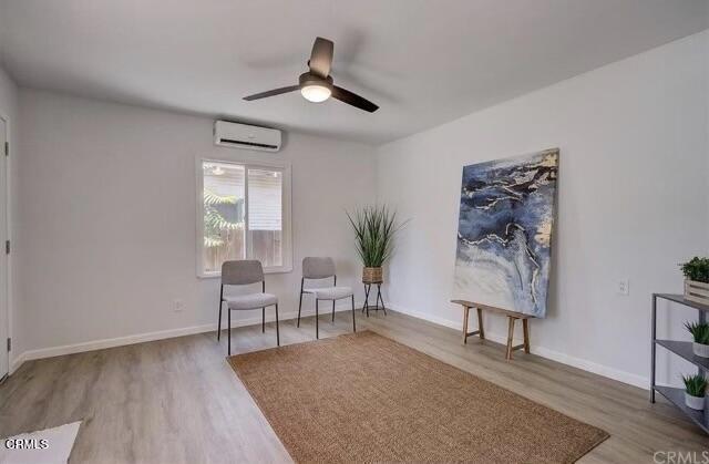 sitting room with ceiling fan, hardwood / wood-style flooring, and a wall unit AC