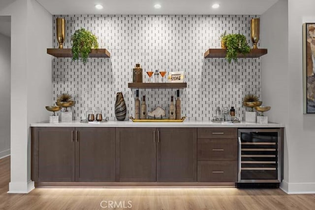 bar featuring dark brown cabinets, decorative backsplash, wine cooler, and light hardwood / wood-style flooring