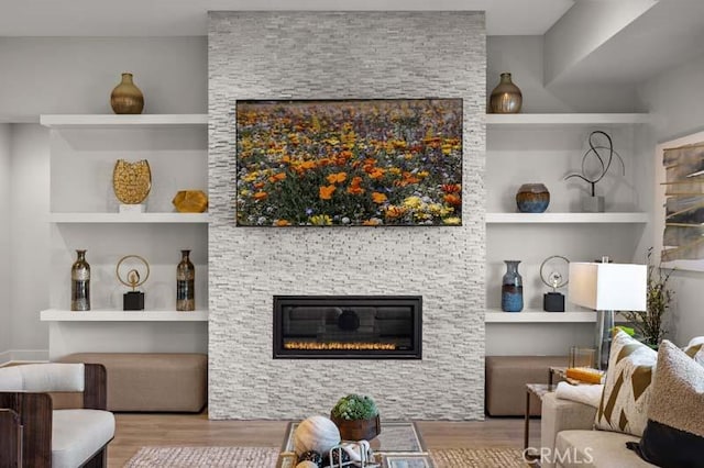 living room with light hardwood / wood-style floors, built in features, and a stone fireplace