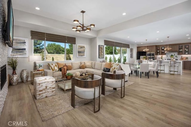 living room featuring light hardwood / wood-style floors, a stone fireplace, and a notable chandelier