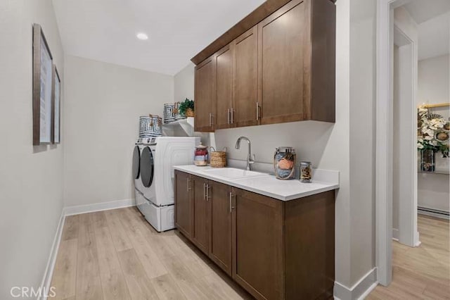 washroom with light hardwood / wood-style floors, sink, washing machine and clothes dryer, and cabinets