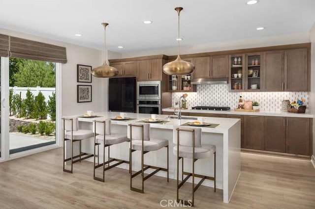 kitchen with stainless steel microwave, gas cooktop, light hardwood / wood-style floors, and pendant lighting