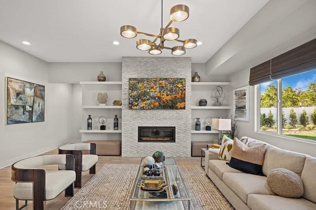 living room featuring built in shelves, light wood-type flooring, a notable chandelier, and a stone fireplace