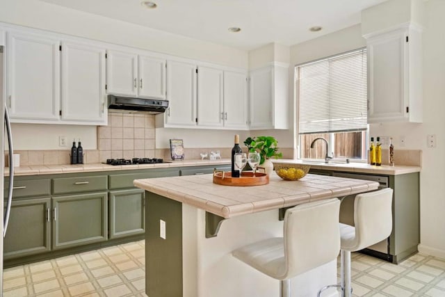 kitchen featuring tile counters, white cabinetry, black gas cooktop, green cabinetry, and a breakfast bar