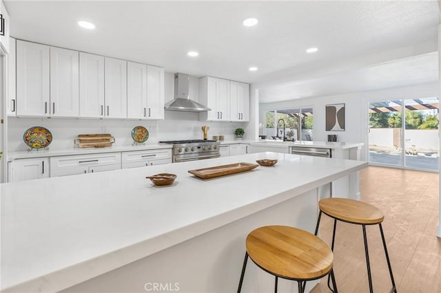 kitchen featuring a kitchen breakfast bar, appliances with stainless steel finishes, white cabinets, wall chimney range hood, and sink