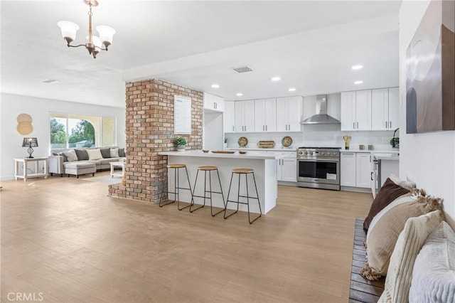 kitchen featuring stainless steel stove, wall chimney exhaust hood, light hardwood / wood-style flooring, decorative light fixtures, and white cabinets